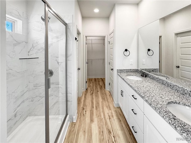 full bath with a sink, a spacious closet, double vanity, wood finished floors, and a marble finish shower