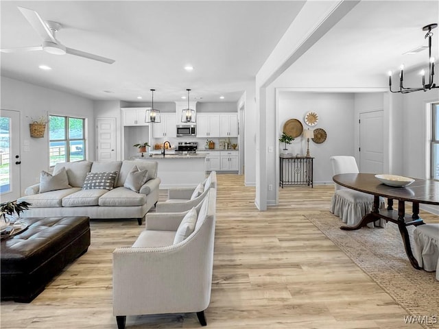 living room with recessed lighting, light wood-type flooring, baseboards, and ceiling fan with notable chandelier