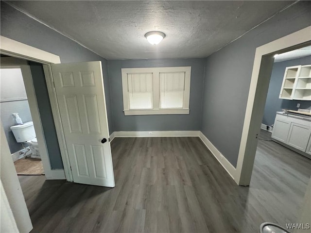 unfurnished bedroom featuring baseboards, a textured ceiling, and dark wood-style flooring