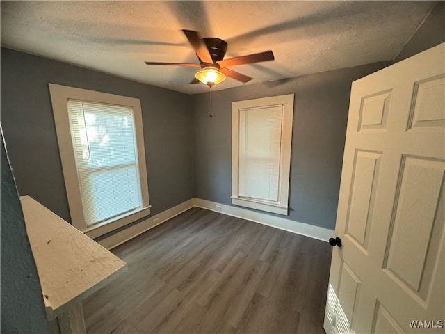 unfurnished bedroom featuring a textured ceiling, dark wood-type flooring, baseboards, and a ceiling fan