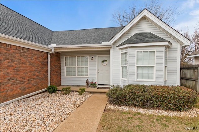 doorway to property with covered porch, fence, brick siding, and roof with shingles