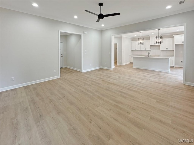 unfurnished living room featuring ornamental molding, sink, ceiling fan with notable chandelier, and light hardwood / wood-style flooring