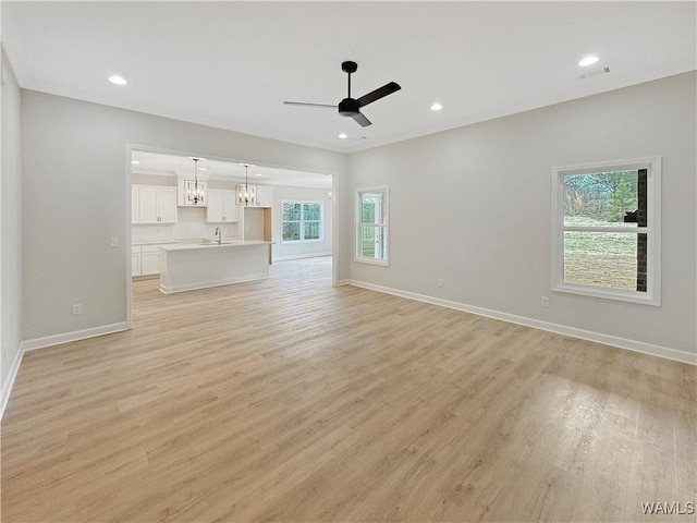 unfurnished living room featuring ceiling fan with notable chandelier and light wood-type flooring