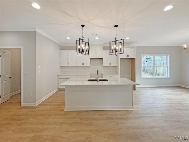 kitchen with sink, light stone counters, decorative light fixtures, an island with sink, and white cabinets