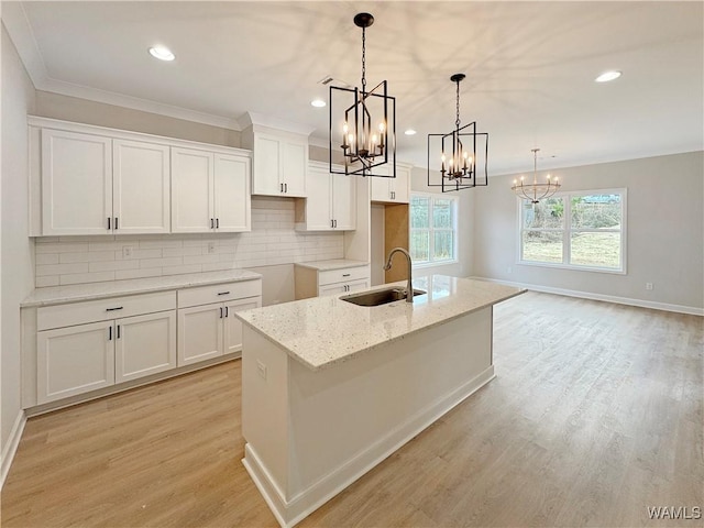 kitchen with decorative light fixtures, white cabinetry, sink, a kitchen island with sink, and light stone countertops