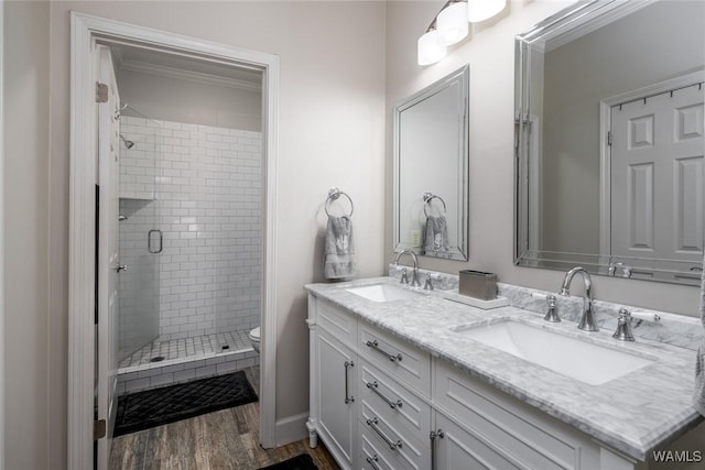 full bath featuring double vanity, a stall shower, a sink, and wood finished floors