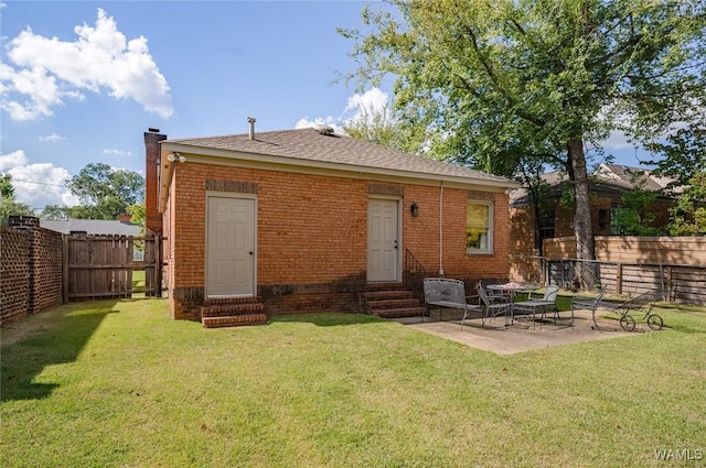 rear view of house featuring entry steps, a lawn, a fenced backyard, a chimney, and brick siding