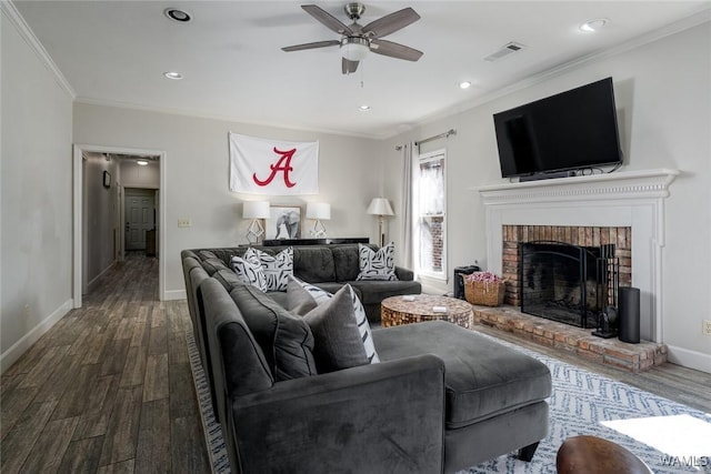 living room with wood finished floors, visible vents, baseboards, ornamental molding, and a brick fireplace