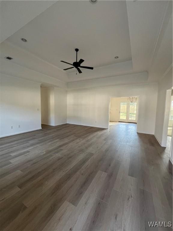 unfurnished living room featuring hardwood / wood-style flooring, ceiling fan, and a tray ceiling