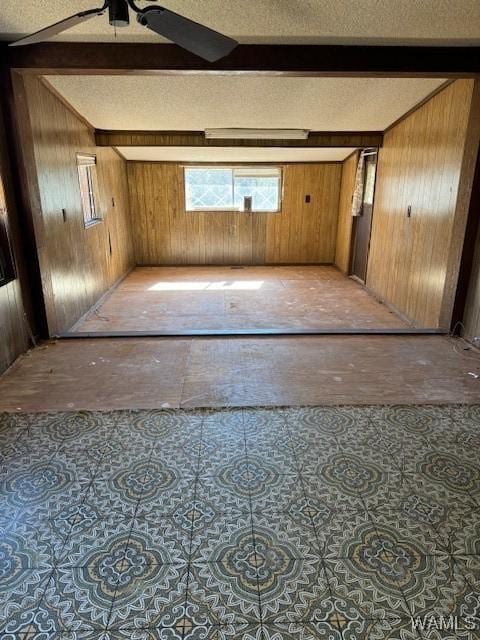 empty room with ceiling fan, beamed ceiling, and wood walls