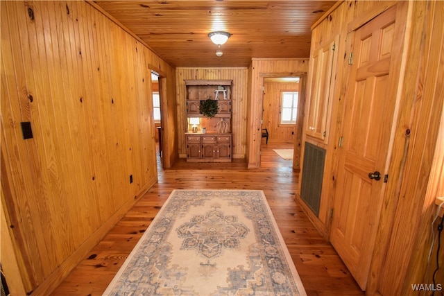 corridor with wood walls, light wood-type flooring, and wooden ceiling