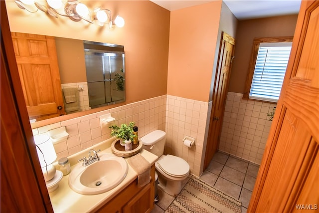 bathroom featuring vanity, a shower with door, tile walls, tile patterned flooring, and toilet