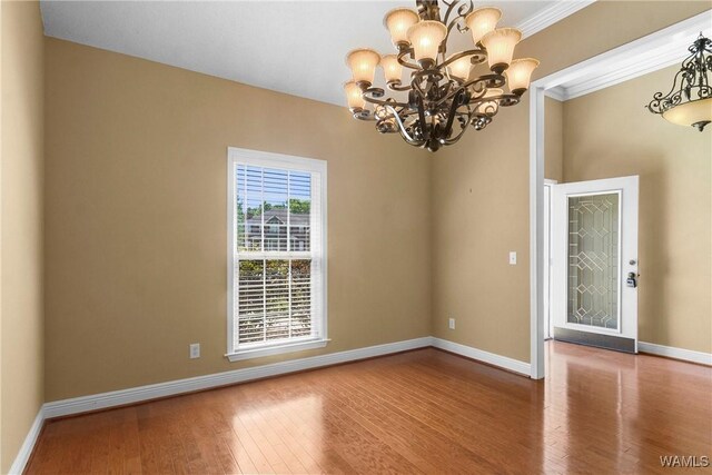 spare room with hardwood / wood-style flooring, crown molding, baseboards, and a chandelier