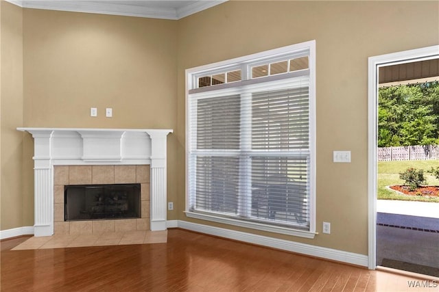 unfurnished living room featuring ornamental molding, a tile fireplace, baseboards, and wood finished floors