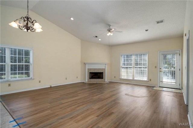 unfurnished living room with ceiling fan with notable chandelier, hardwood / wood-style floors, lofted ceiling, a tiled fireplace, and a textured ceiling