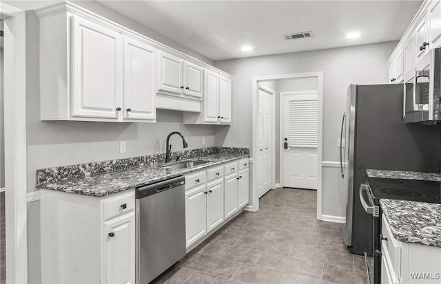 kitchen with white cabinetry, sink, stainless steel appliances, dark stone counters, and light tile patterned floors