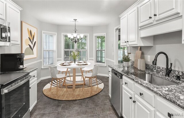 kitchen featuring white cabinetry, sink, stainless steel appliances, dark stone counters, and pendant lighting