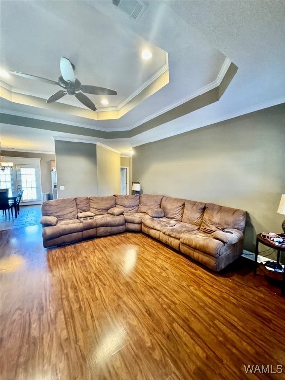 living room featuring ceiling fan, a raised ceiling, wood-type flooring, and crown molding