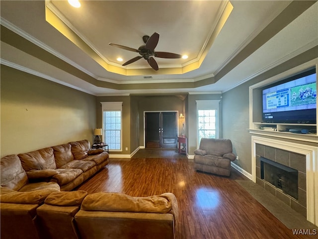 unfurnished living room with a tile fireplace, ceiling fan, dark hardwood / wood-style flooring, crown molding, and a tray ceiling