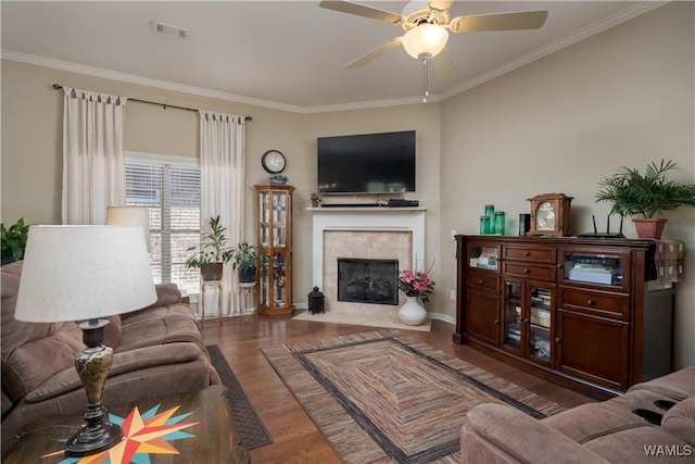 living area featuring visible vents, ornamental molding, a ceiling fan, wood finished floors, and a tile fireplace