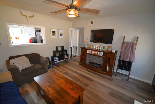 living area with a textured ceiling, dark wood-type flooring, visible vents, baseboards, and a ceiling fan