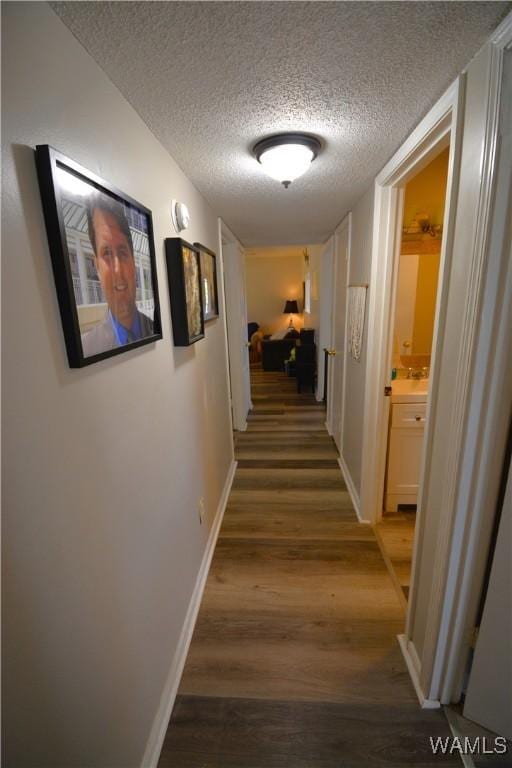 hall featuring dark wood-style flooring, a textured ceiling, and baseboards