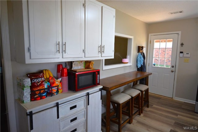 kitchen featuring light countertops, white cabinets, visible vents, and light wood finished floors