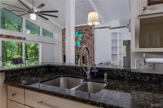 kitchen featuring decorative light fixtures, white cabinetry, dark stone countertops, sink, and lofted ceiling with beams