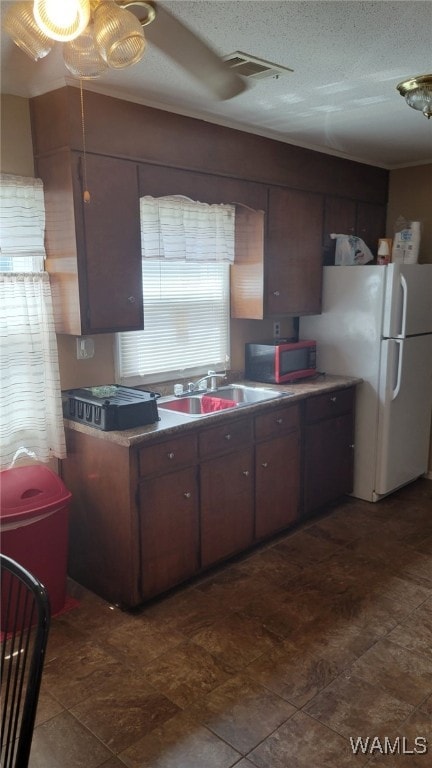 kitchen featuring a textured ceiling, dark brown cabinets, white refrigerator, and sink