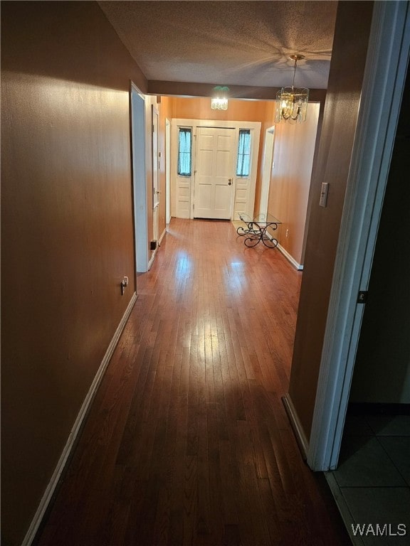 hall with hardwood / wood-style floors, a textured ceiling, and an inviting chandelier