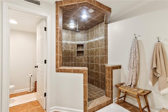 bathroom with tile patterned flooring, crown molding, toilet, and tiled shower