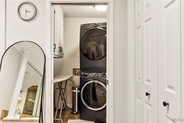 washroom featuring stacked washer / drying machine and dark tile patterned flooring