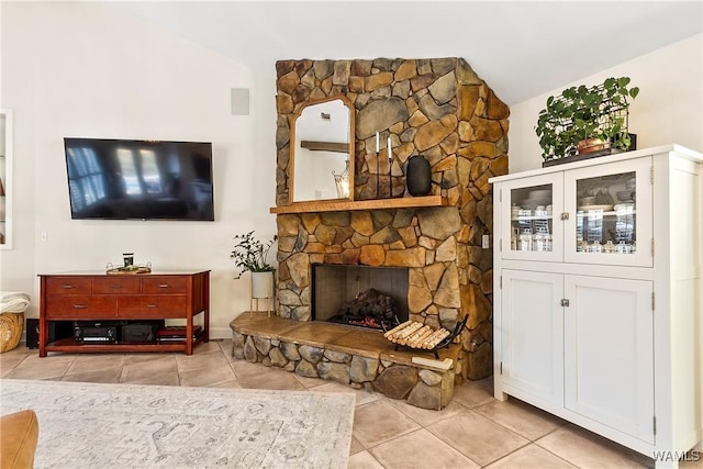 living room with vaulted ceiling, a stone fireplace, and light tile patterned flooring