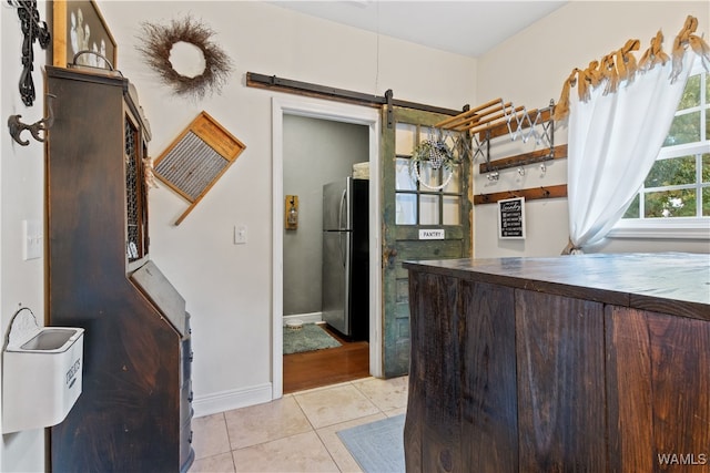 kitchen featuring a barn door, light tile patterned flooring, dark brown cabinetry, and stainless steel refrigerator