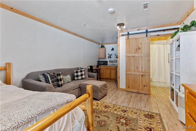 bedroom featuring a barn door, light hardwood / wood-style floors, and crown molding