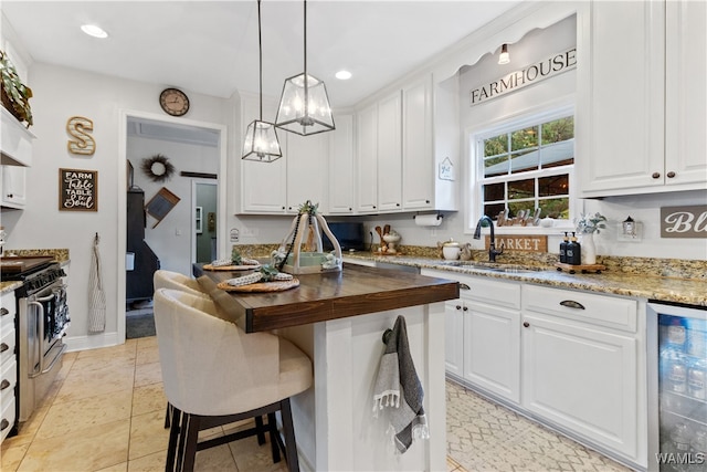 kitchen featuring gas stove, wine cooler, butcher block countertops, decorative light fixtures, and white cabinets