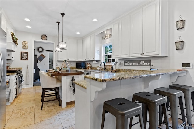 kitchen with kitchen peninsula, dark stone counters, decorative light fixtures, a breakfast bar, and white cabinets