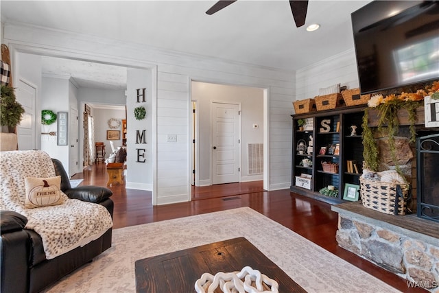 living room featuring hardwood / wood-style floors, ceiling fan, a stone fireplace, and ornamental molding