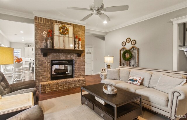 living room featuring hardwood / wood-style floors, ceiling fan, crown molding, and a brick fireplace