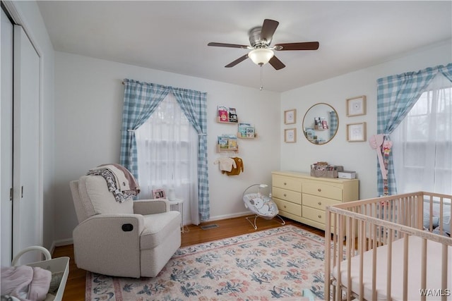 bedroom with a nursery area, ceiling fan, multiple windows, and hardwood / wood-style flooring