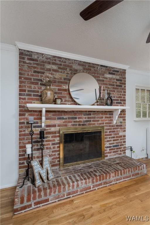 details with crown molding, a brick fireplace, a textured ceiling, ceiling fan, and hardwood / wood-style floors