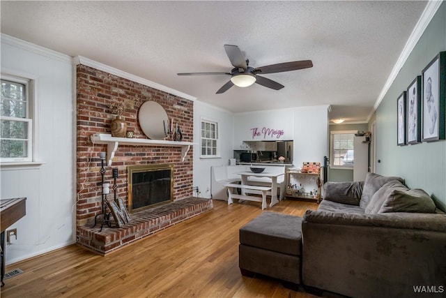 living room featuring a fireplace, wood-type flooring, ornamental molding, and a textured ceiling