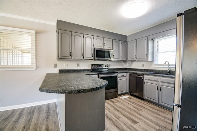 kitchen with kitchen peninsula, appliances with stainless steel finishes, light wood-type flooring, a textured ceiling, and sink