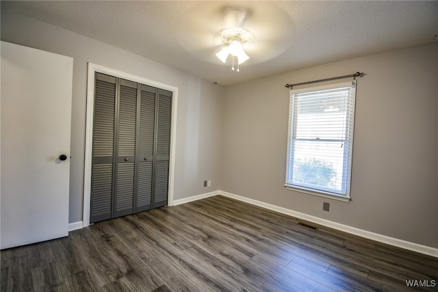 unfurnished bedroom with a textured ceiling, ceiling fan, dark wood-type flooring, and a closet