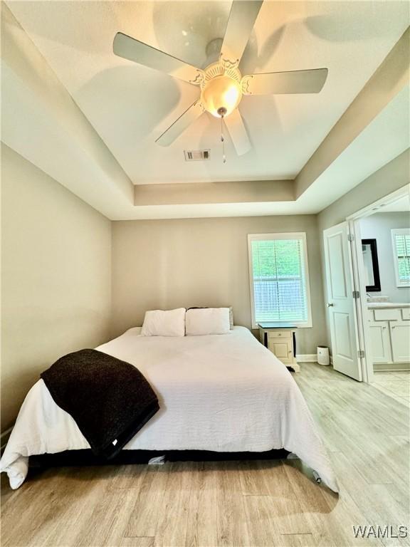 6643 Cooperstown Cir, Tuscaloosa, AL 35453 - bedroom featuring a tray ceiling, light wood-style flooring, multiple windows, and connected bathroom