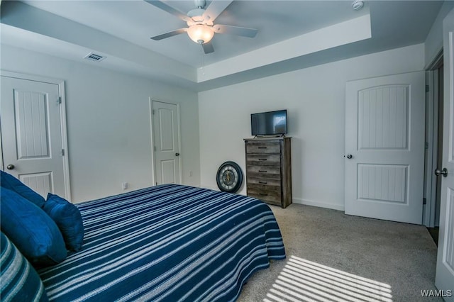 carpeted bedroom featuring visible vents, a tray ceiling, ceiling fan, and baseboards