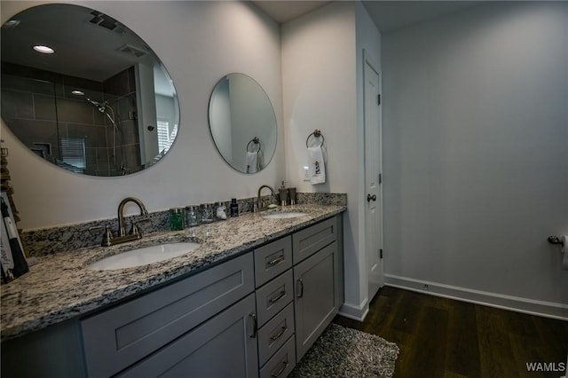 bathroom featuring baseboards, a tile shower, a sink, and wood finished floors