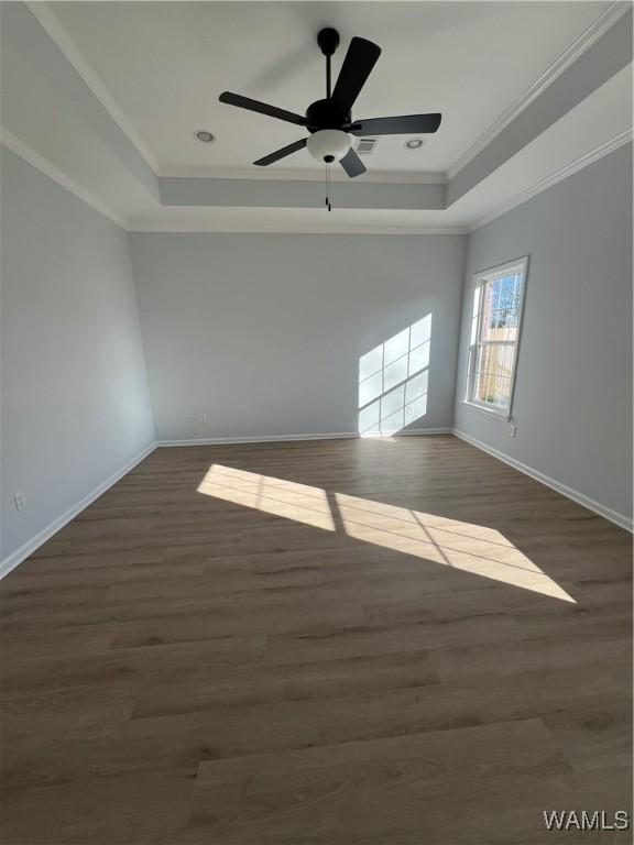 unfurnished room with a tray ceiling, ceiling fan, dark wood-type flooring, and ornamental molding