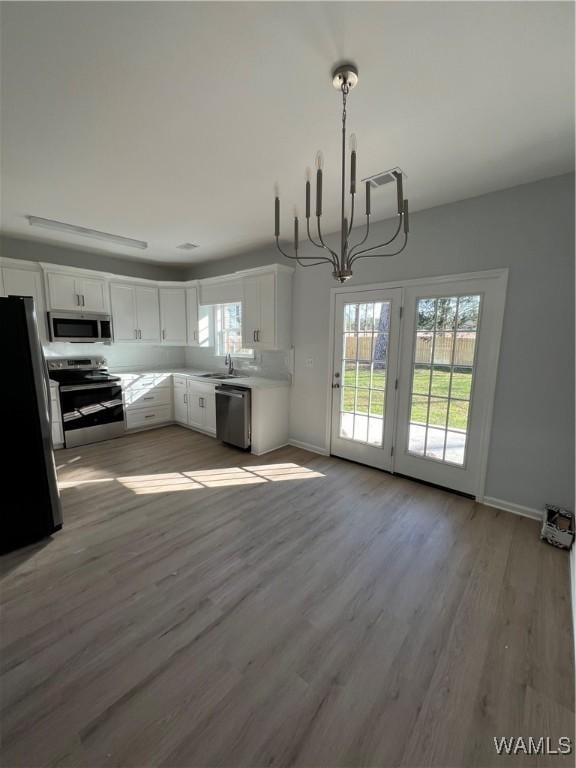 kitchen featuring stainless steel appliances, light hardwood / wood-style flooring, a notable chandelier, white cabinets, and hanging light fixtures