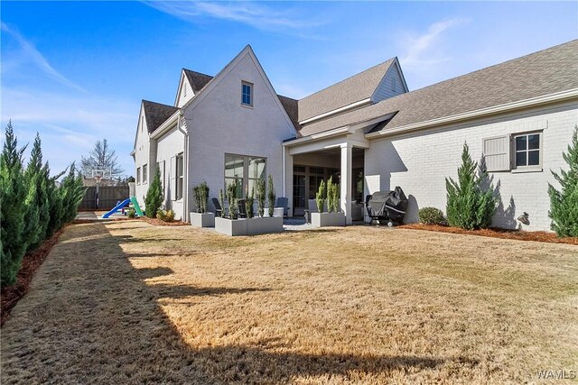 back of house featuring a yard, brick siding, a shingled roof, and fence